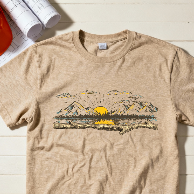 Beige t-shirt with mountain and sun graphic on a wooden surface with hard hat, boots, and gloves.